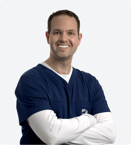 Dr. Rothenberg smiling at the camera with his blue scrubs on and long white sleeve and arms crossed